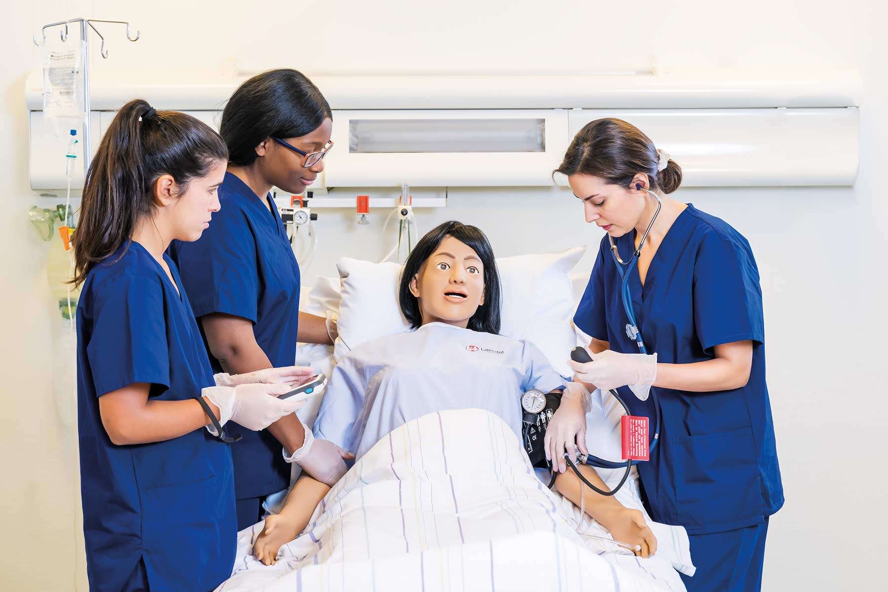 three nurses taking blood pressure on nursing anne simulator with simpad